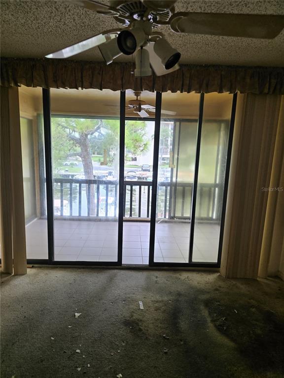 A room with stained carpet and a ceiling fan overlooks a balcony and marina view — 1802 MARINER DR UNIT 32, TARPON SPRINGS, FL