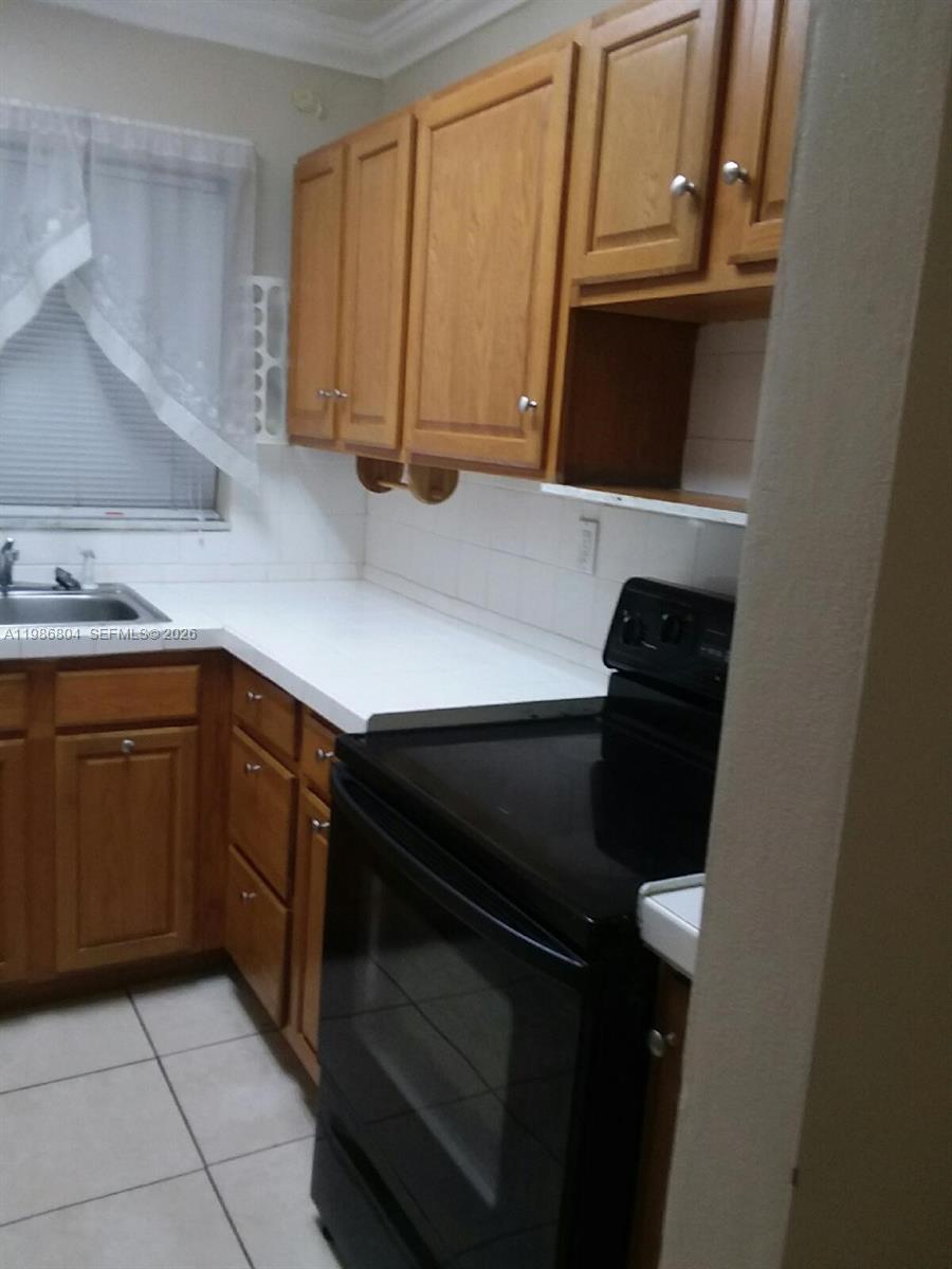 A kitchen features light wood cabinets, white countertops, a black stove, and a window — 140 Royal Palm Rd # 107, Hialeah Gardens FL 33016, HIALEAH GARDENS, FL
