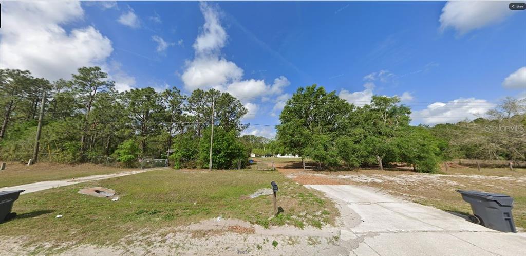 A vacant, grassy lot with a concrete driveway and mature trees under a blue sky — COMMONWEALTH AVE N, POLK CITY, FL