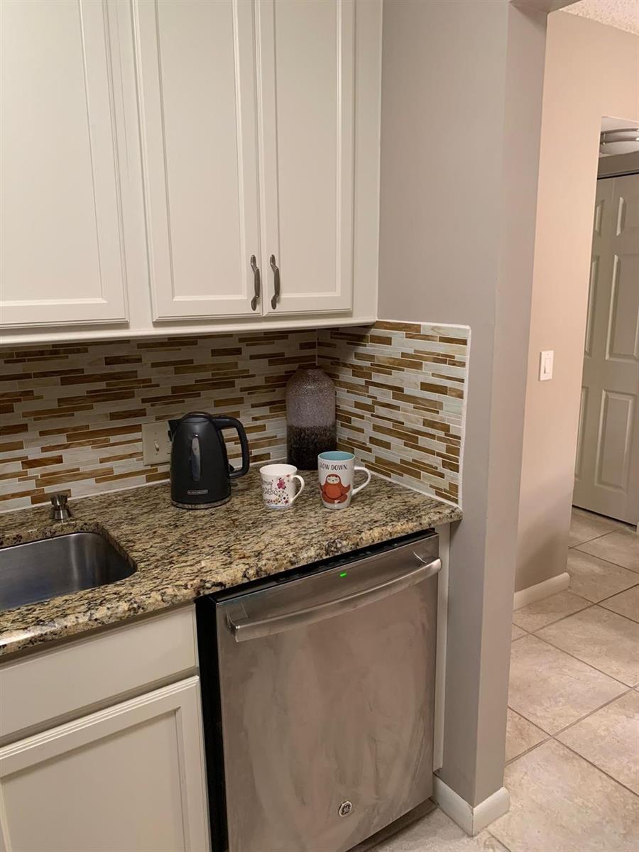 A kitchen features white cabinets, a granite countertop, a stainless steel dishwasher, and tiled backsplash — 87 FANSHAW C # 87, Boca Raton FL 33434, BOCA RATON, FL