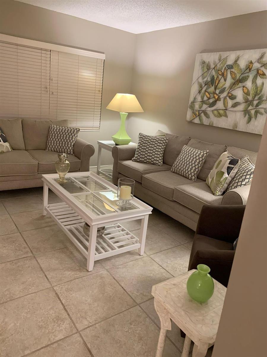 A living room features two beige sofas, a white coffee table, and a green lamp — 87 FANSHAW C # 87, Boca Raton FL 33434, BOCA RATON, FL