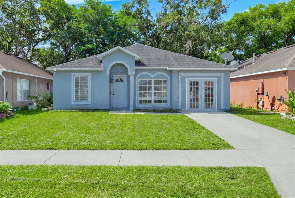 A single-story blue house with a front porch, a concrete driveway, and a grassy lawn — 7544 PINE FORK DRIVE, ORLANDO, FL