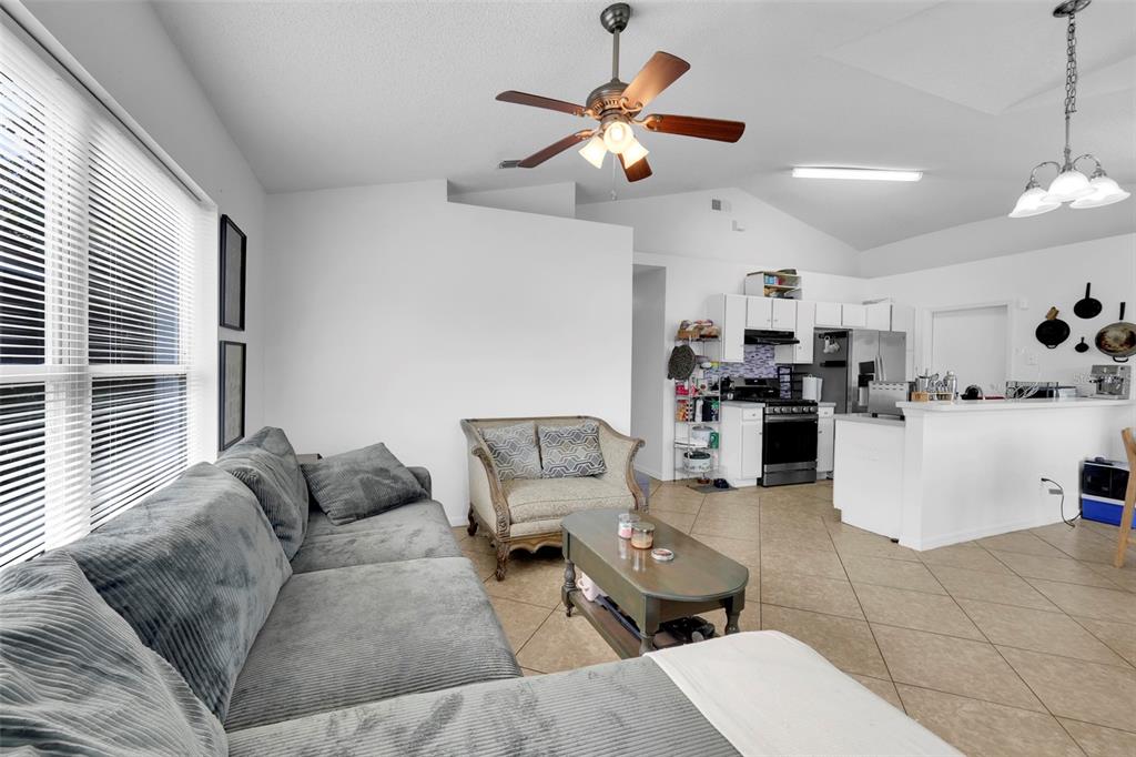 A living room with tile floors, a gray sectional sofa, and an open-concept kitchen — 7544 PINE FORK DRIVE, ORLANDO, FL