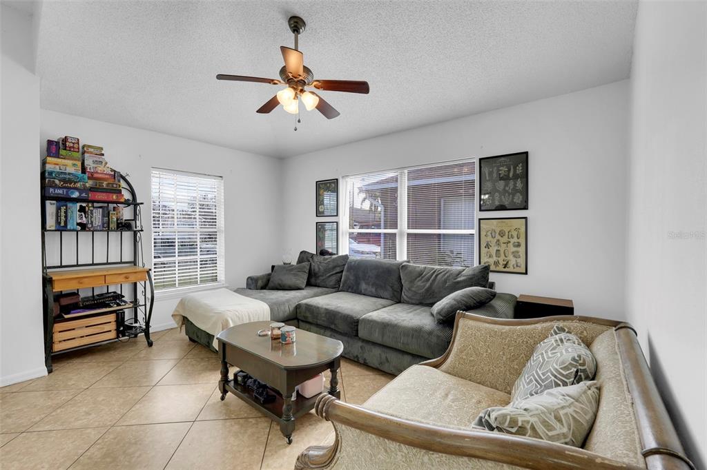 A living room features a gray sectional sofa, a patterned loveseat, and a tall game shelf — 7544 PINE FORK DRIVE, ORLANDO, FL