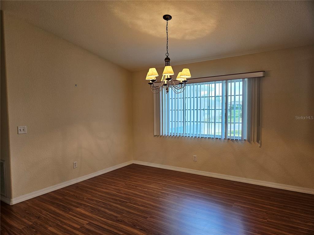 An empty dining room features wood-look flooring, a chandelier, and a window with vertical blinds — 5954 SW 98TH STREET ROAD, OCALA, FL