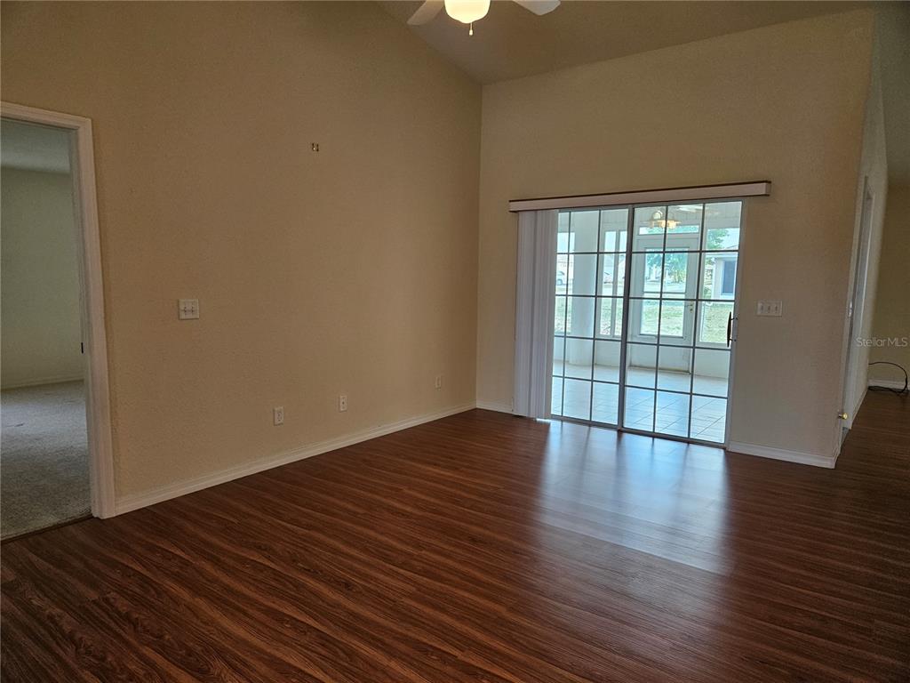 A living room with wood-look flooring, vaulted ceilings, and sliding glass doors to a patio — 5954 SW 98TH STREET ROAD, OCALA, FL