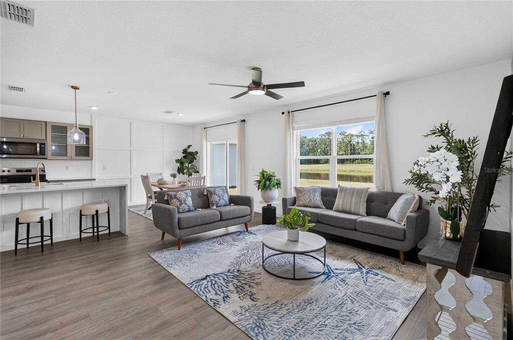 An open-concept living room and kitchen featuring gray sofas, a coastal rug, and large windows — 1037 CHAMPION RDG DRIVE, DAYTONA BEACH, FL