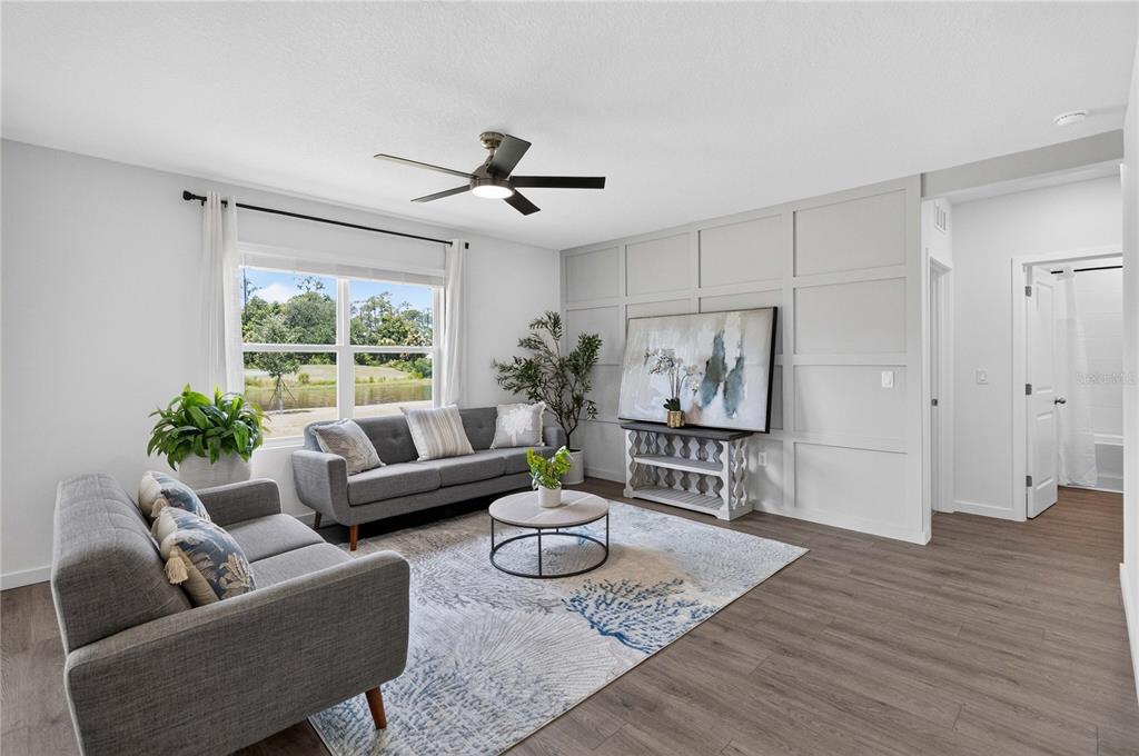 A living room features gray sofas, a patterned rug, and a paneled accent wall — 1037 CHAMPION RDG DRIVE, DAYTONA BEACH, FL