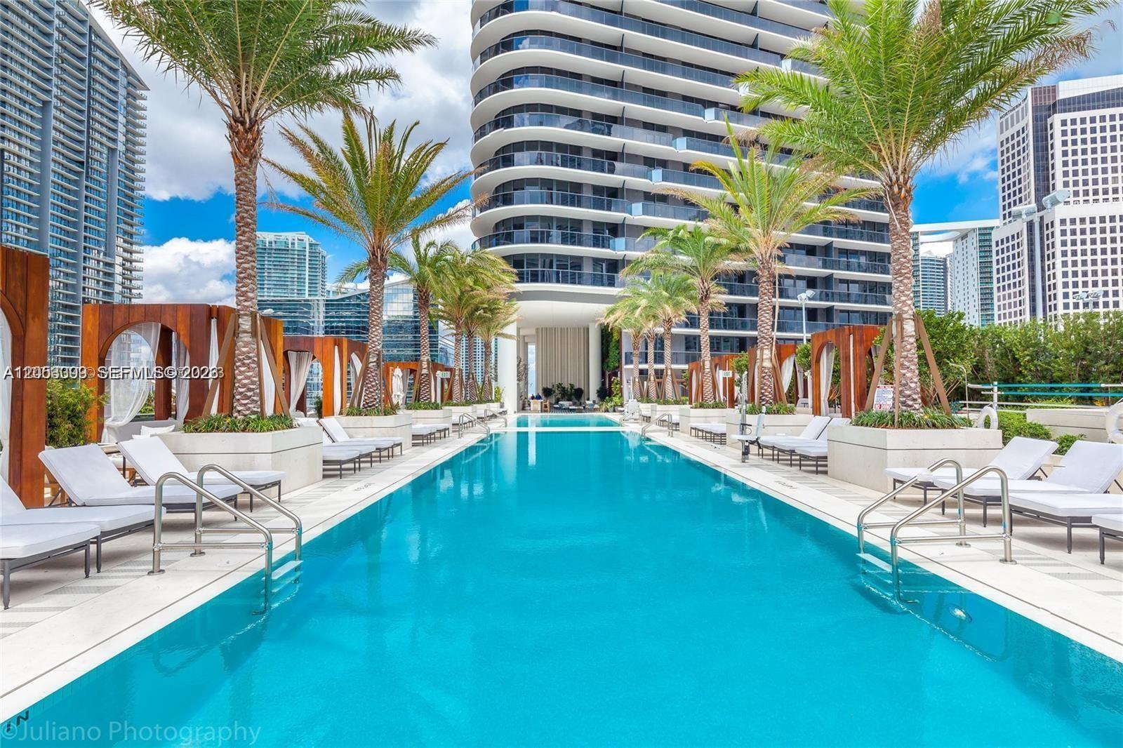 A long swimming pool is surrounded by lounge chairs, palm trees, and wooden cabanas — 801 S Miami Ave # 3006, Miami FL 33130, MIAMI, FL