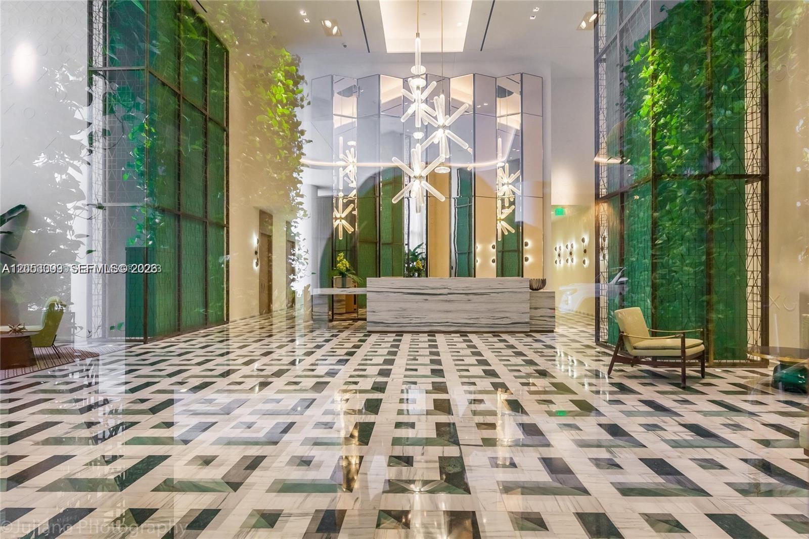 A modern lobby features a marble reception desk, geometric patterned flooring, and tall green walls — 801 S Miami Ave # 3006, Miami FL 33130, MIAMI, FL