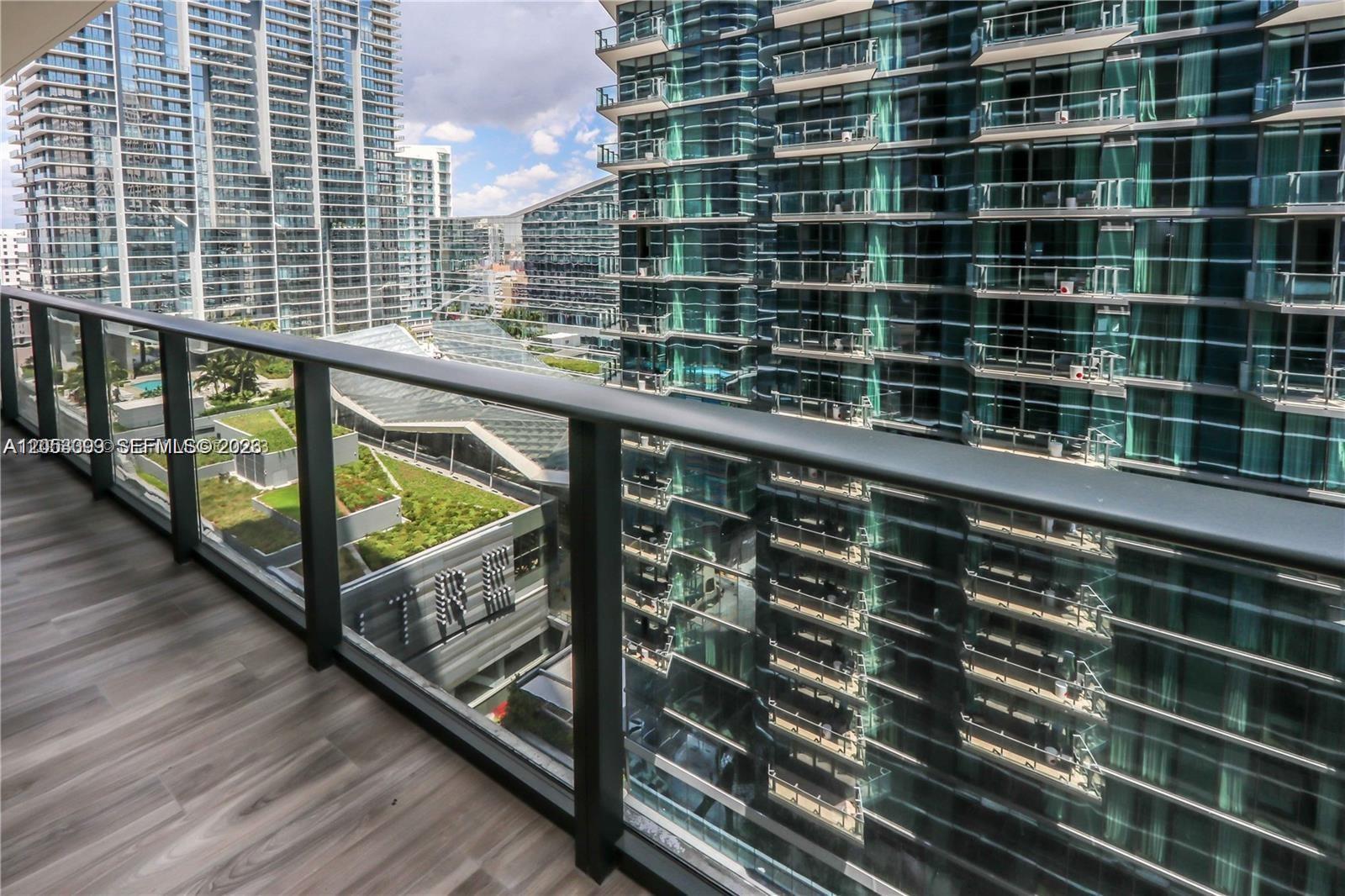 A balcony with a glass railing overlooks modern high-rise buildings and a green roof — 801 S Miami Ave # 3006, Miami FL 33130, MIAMI, FL