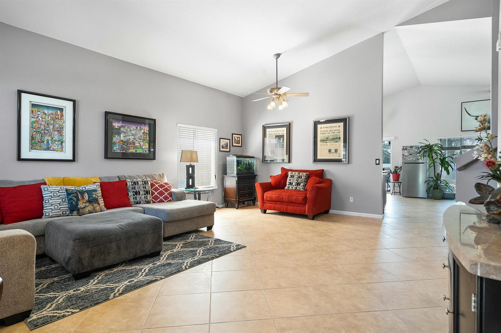 A living room with tile flooring, a gray sectional sofa, a red armchair, and vaulted ceilings — 2480 SE Springtree Place, Stuart FL 34997, STUART, FL