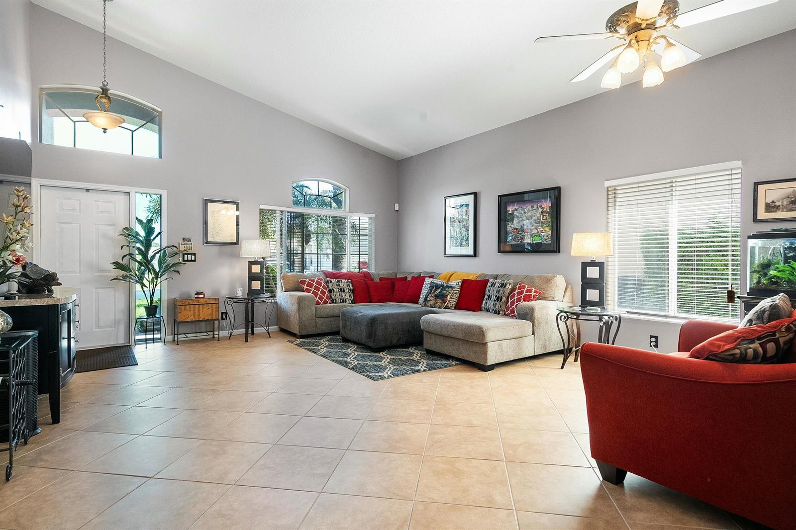 A living room features light gray walls, tile flooring, a sectional sofa, and a red armchair — 2480 SE Springtree Place, Stuart FL 34997, STUART, FL