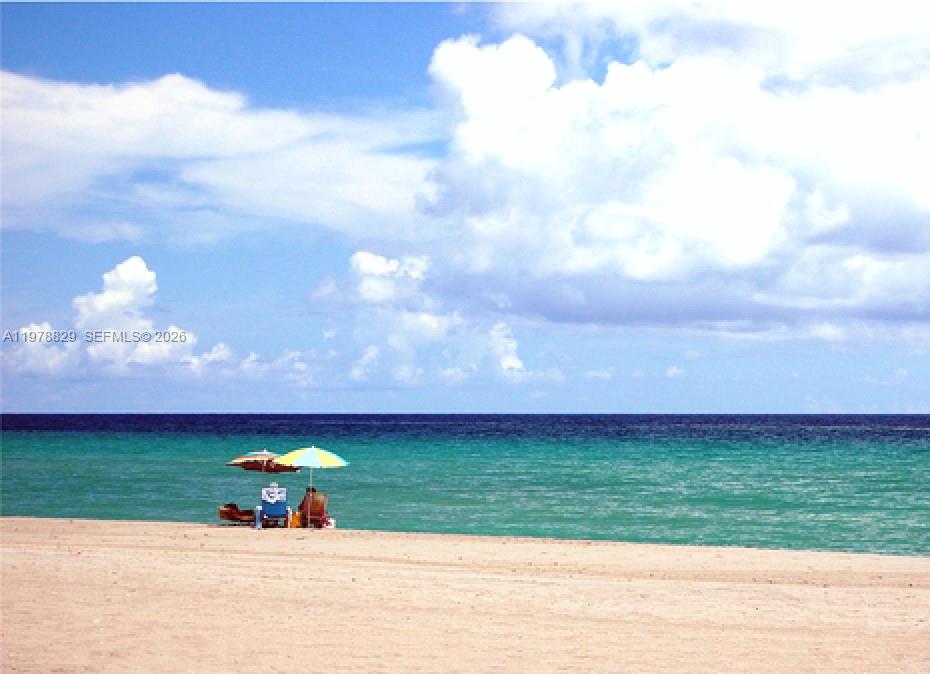 A person sits under a beach umbrella on a sandy shore overlooking the ocean — 140 S Dixie Hwy # 719, Hollywood FL 33020, HOLLYWOOD, FL