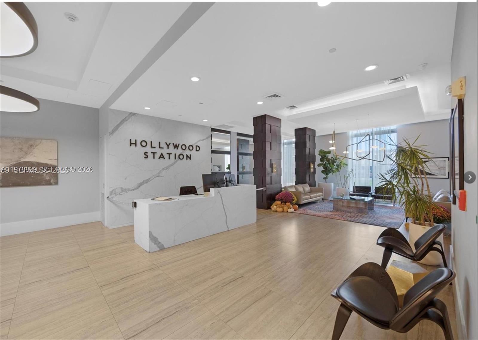 A modern lobby features a marble reception desk, wood-look tile flooring, and a seating area — 140 S Dixie Hwy # 719, Hollywood FL 33020, HOLLYWOOD, FL