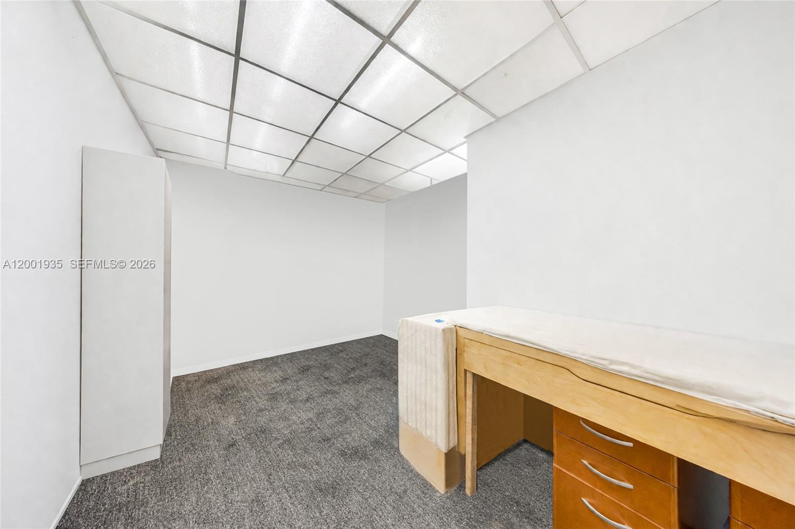 A small room features a drop ceiling, gray carpet, a white cabinet, and a desk — 5401 Collins Ave # 9, Miami Beach FL 33140, MIAMI BEACH, FL