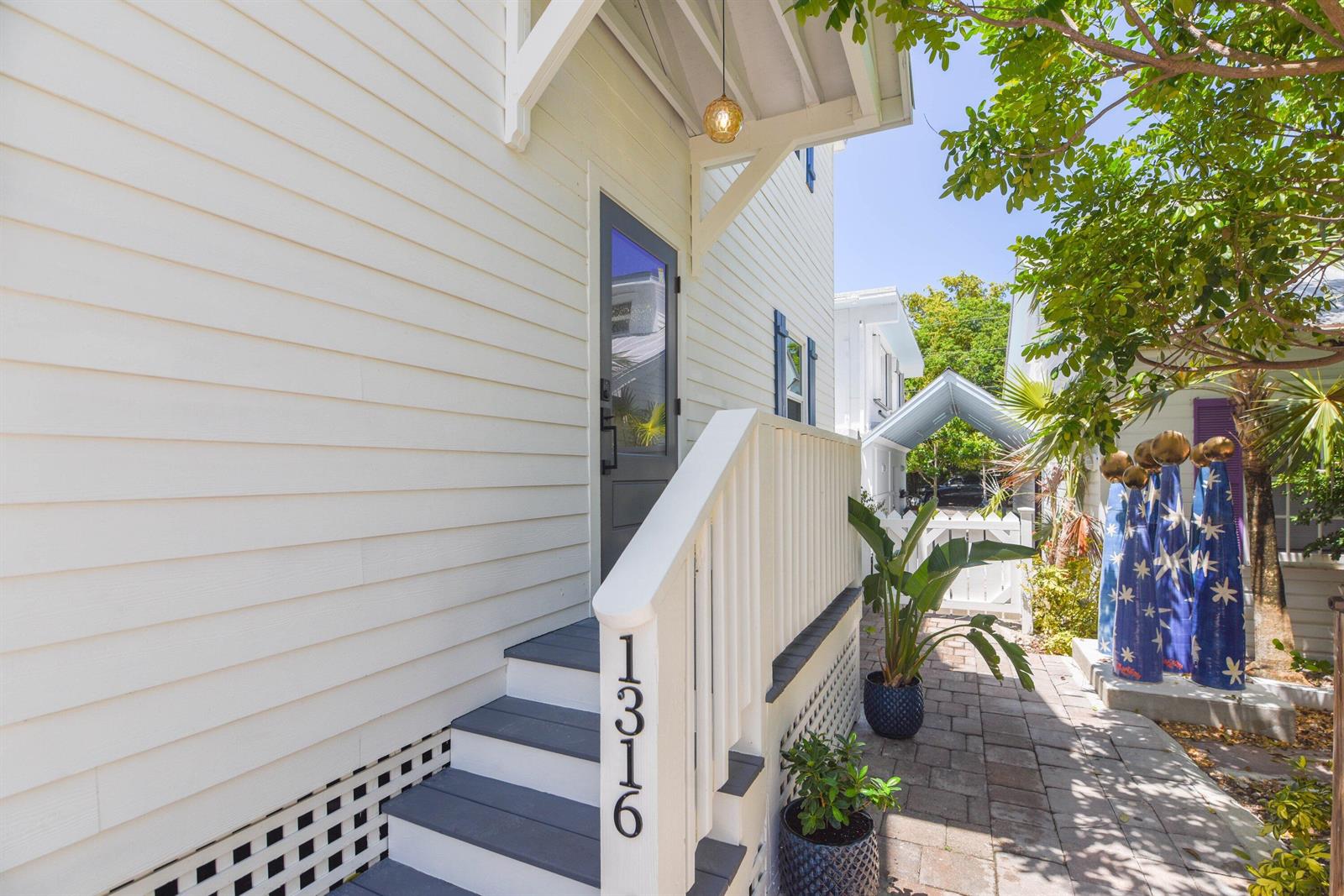 An exterior view shows a house entrance with white siding, a grey door, and stairs — 1316 Royal Street # 6, Key West FL 33040, KEY WEST, FL