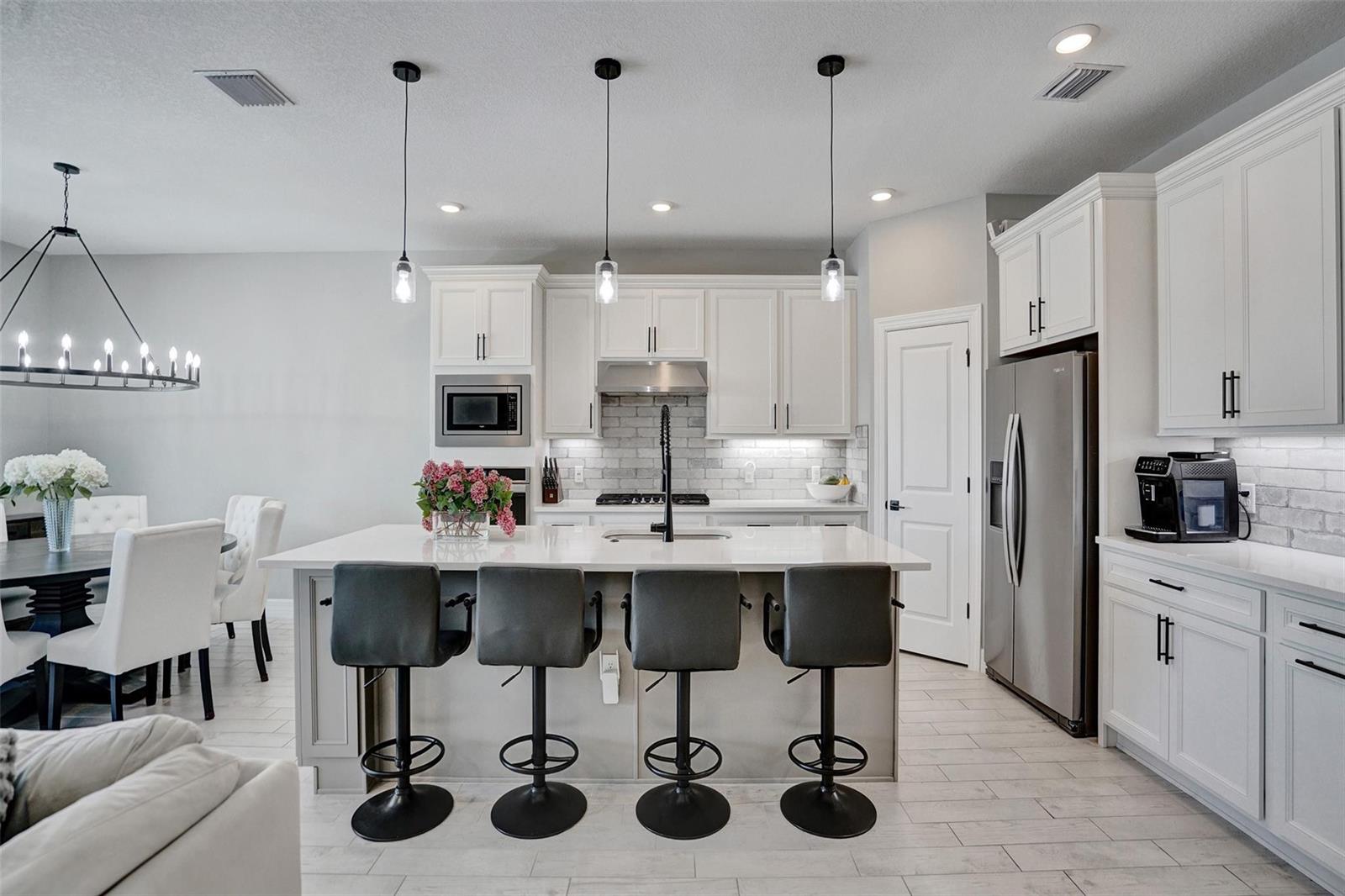 A modern kitchen features white cabinetry, a central island with four barstools, and stainless appliances — 9621 Mosler Trail, Lake Worth FL 33467, LAKE WORTH, FL