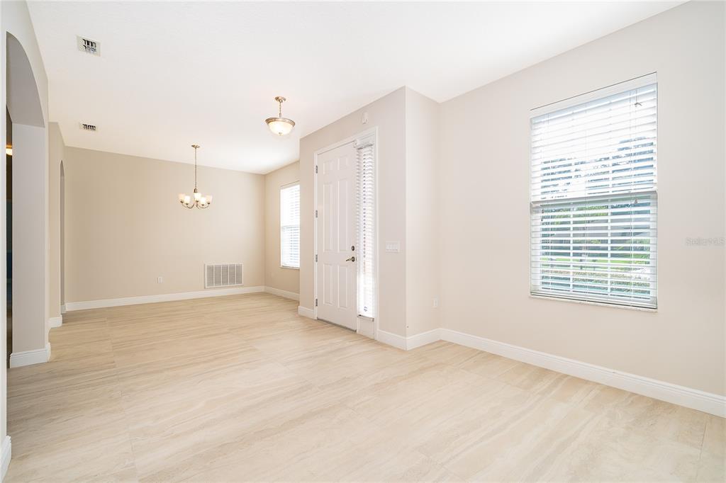 An empty room with light-colored tile flooring, a white front door, and a large window — 700 ELKHORN FERN LANE, DELAND, FL