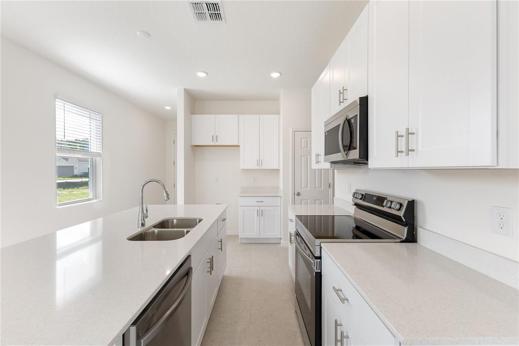A modern kitchen features white cabinets, quartz countertops, stainless steel appliances, and a central island — 9129 WILDLIGHT TRAIL, WILDWOOD, FL