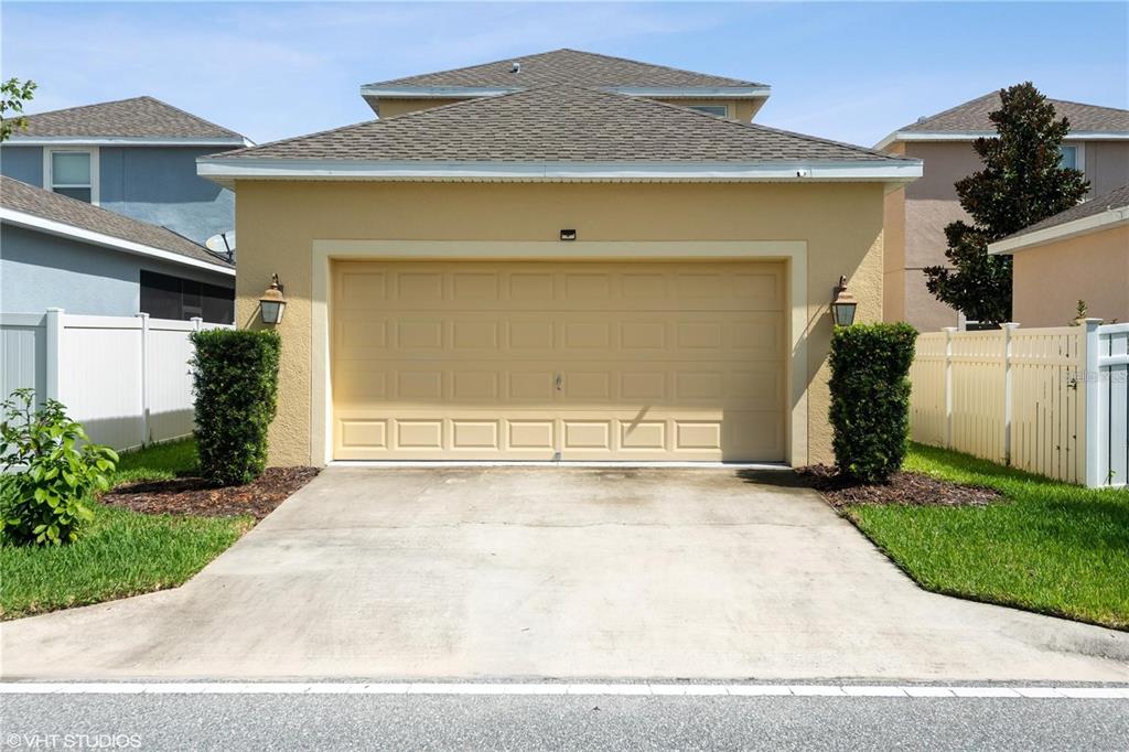 A tan house exterior features a two-car garage, a concrete driveway, and white vinyl fencing — 6814 HABITAT DRIVE, HARMONY, FL