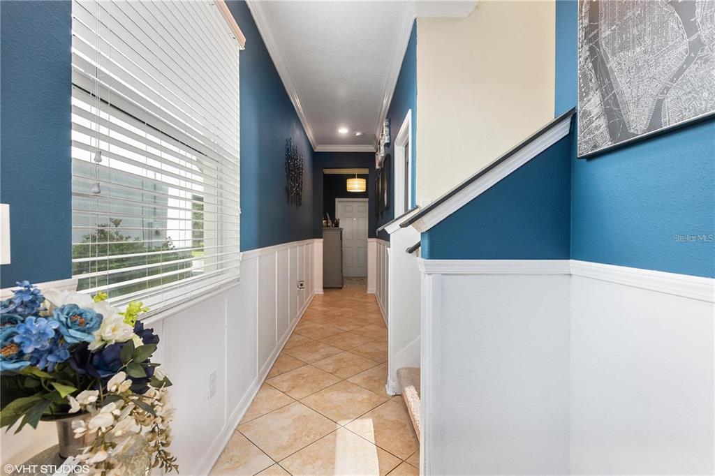 A hallway with blue walls, white wainscoting, and tile flooring leads toward a doorway — 6814 HABITAT DRIVE, HARMONY, FL