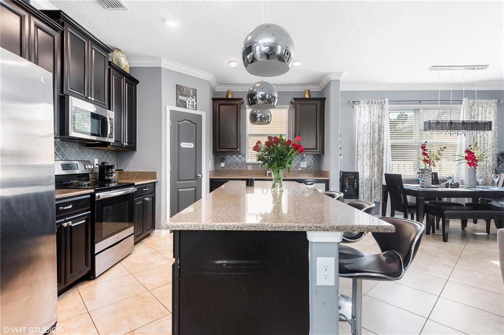 A kitchen features dark wood cabinets, granite countertops, a central island, and stainless steel appliances — 6814 HABITAT DRIVE, HARMONY, FL