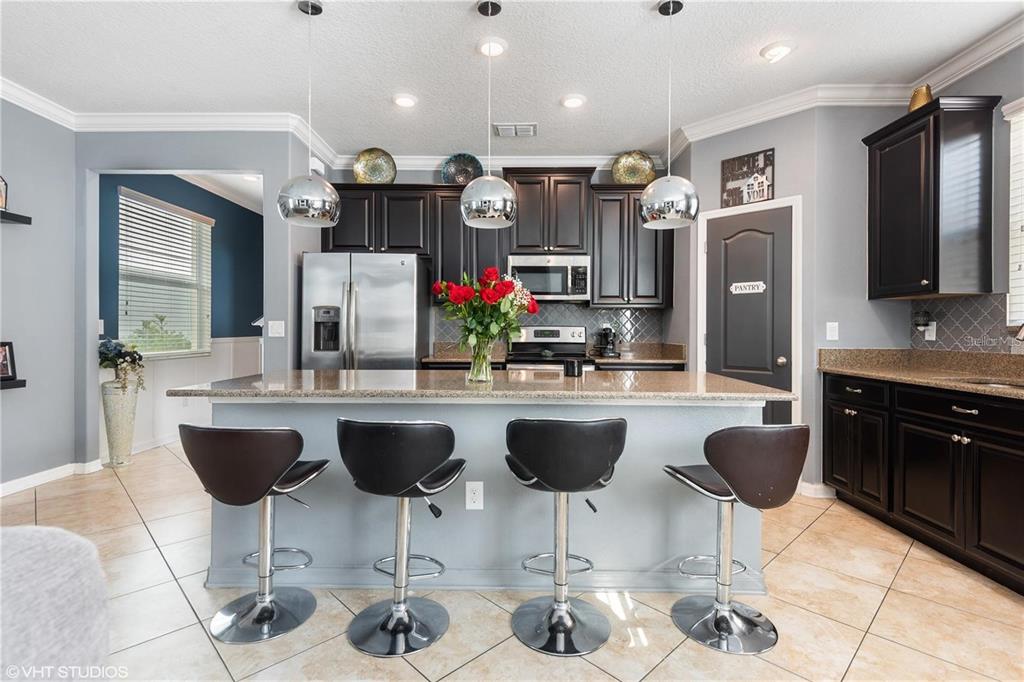 A kitchen features a gray island with four bar stools, dark cabinets, and stainless appliances — 6814 HABITAT DRIVE, HARMONY, FL