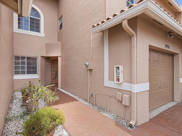 The exterior of a tan stucco building features a walkway, a garage, and a front door — 8596 Jade Drive, Tamarac FL 33321, TAMARAC, FL