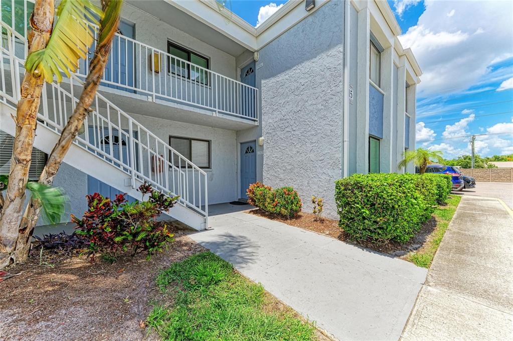 A two-story apartment building exterior features a white staircase, blue doors, and landscaped bushes — 5310 26TH STREET W UNIT 1506, BRADENTON, FL