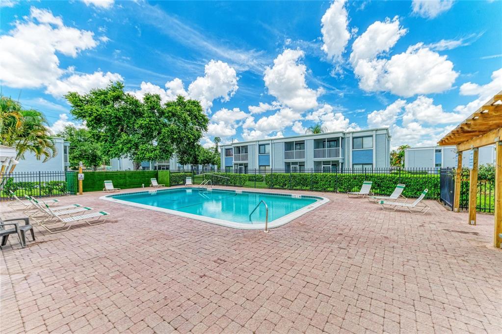 An outdoor swimming pool surrounded by a brick patio, lounge chairs, and apartment buildings — 5310 26TH STREET W UNIT 1506, BRADENTON, FL
