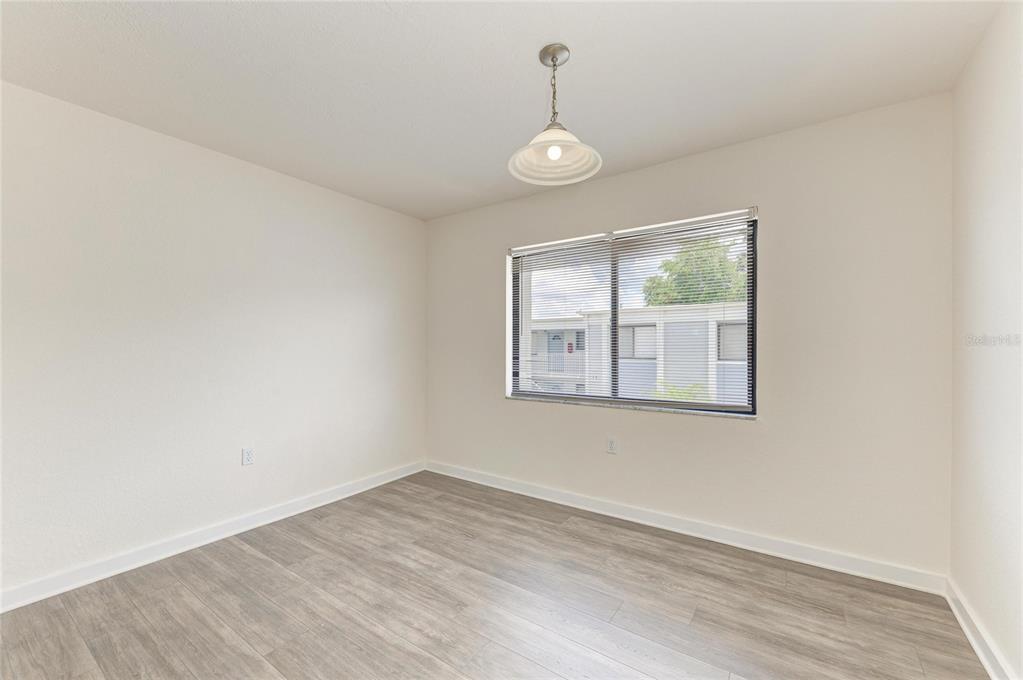 An empty room features light-colored walls, wood-look flooring, a single pendant light, and a window — 5310 26TH STREET W UNIT 1506, BRADENTON, FL