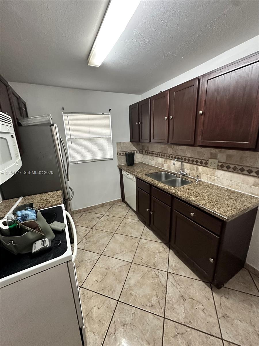 A kitchen features dark wood cabinets, granite countertops, a double sink, and tiled flooring — 4111 Stirling Rd # 408, Dania Beach FL 33314, DANIA BEACH, FL
