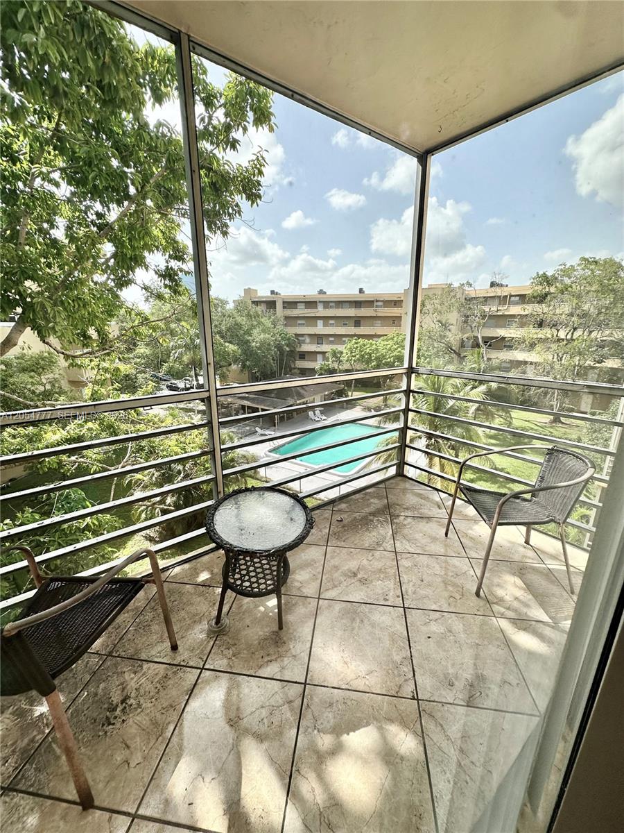 A screened-in balcony with tile flooring overlooks a swimming pool and apartment buildings — 4111 Stirling Rd # 408, Dania Beach FL 33314, DANIA BEACH, FL