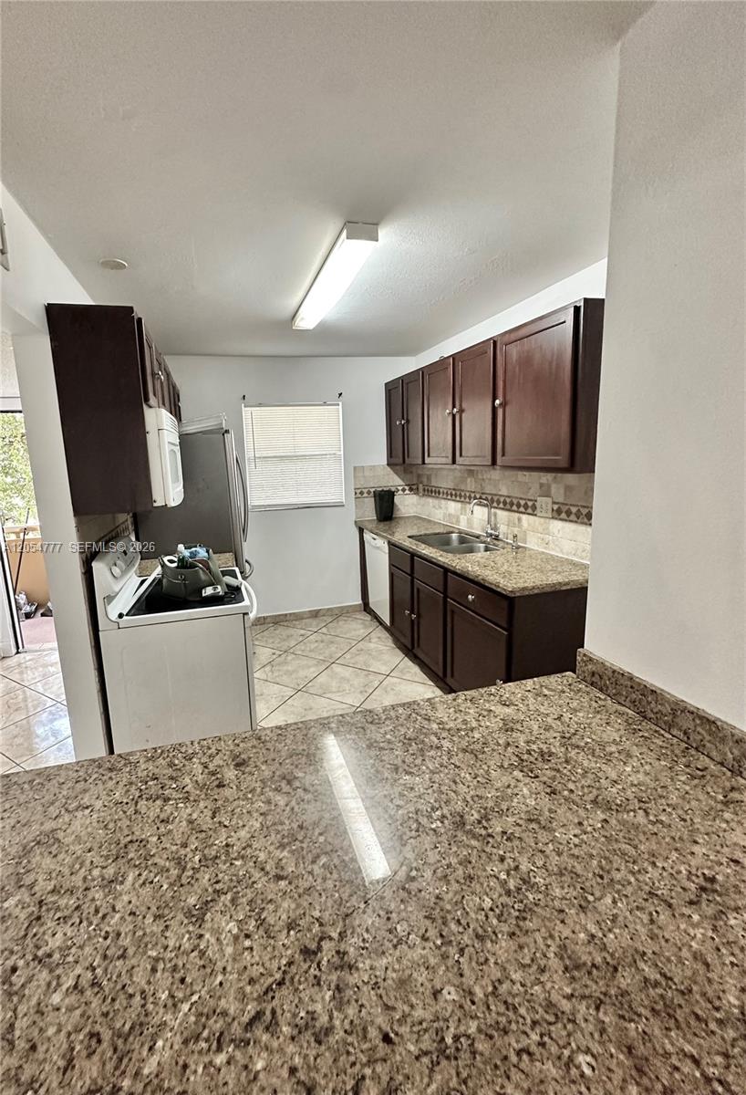 A kitchen features dark wood cabinets, granite countertops, tile flooring, and a window — 4111 Stirling Rd # 408, Dania Beach FL 33314, DANIA BEACH, FL
