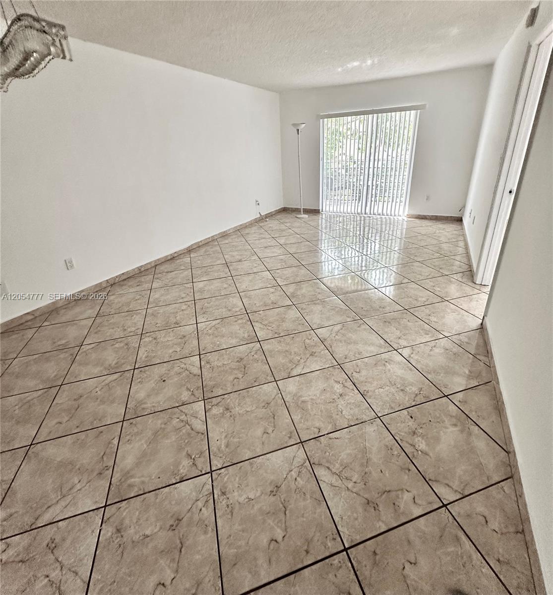 An empty room features beige marble-look tile flooring, white walls, and a sliding glass door — 4111 Stirling Rd # 408, Dania Beach FL 33314, DANIA BEACH, FL