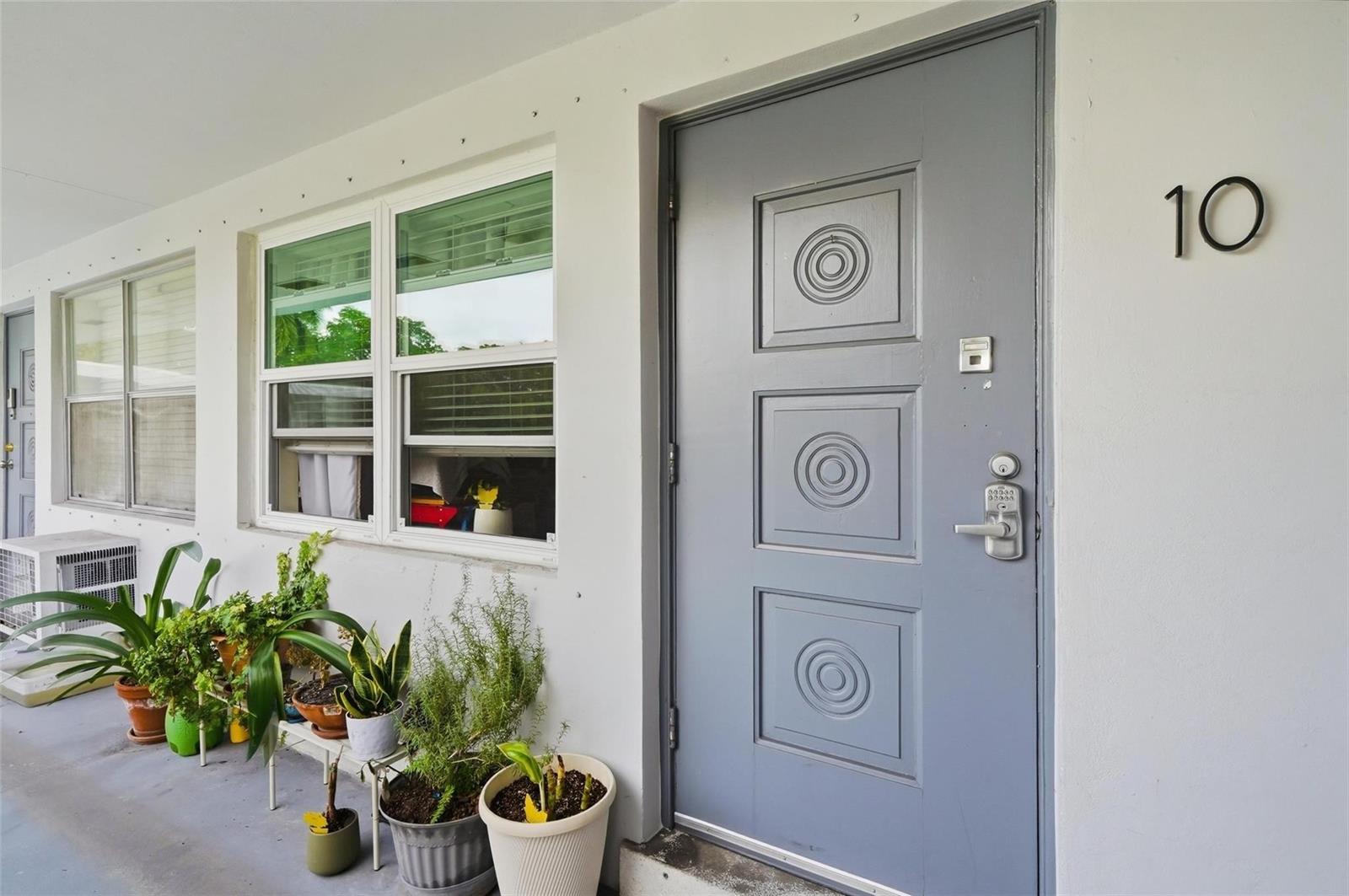 A grey front door with three circular panels and the number ten sits beside potted plants — 3510 Harrison Street # 10, Hollywood FL 33021, HOLLYWOOD, FL