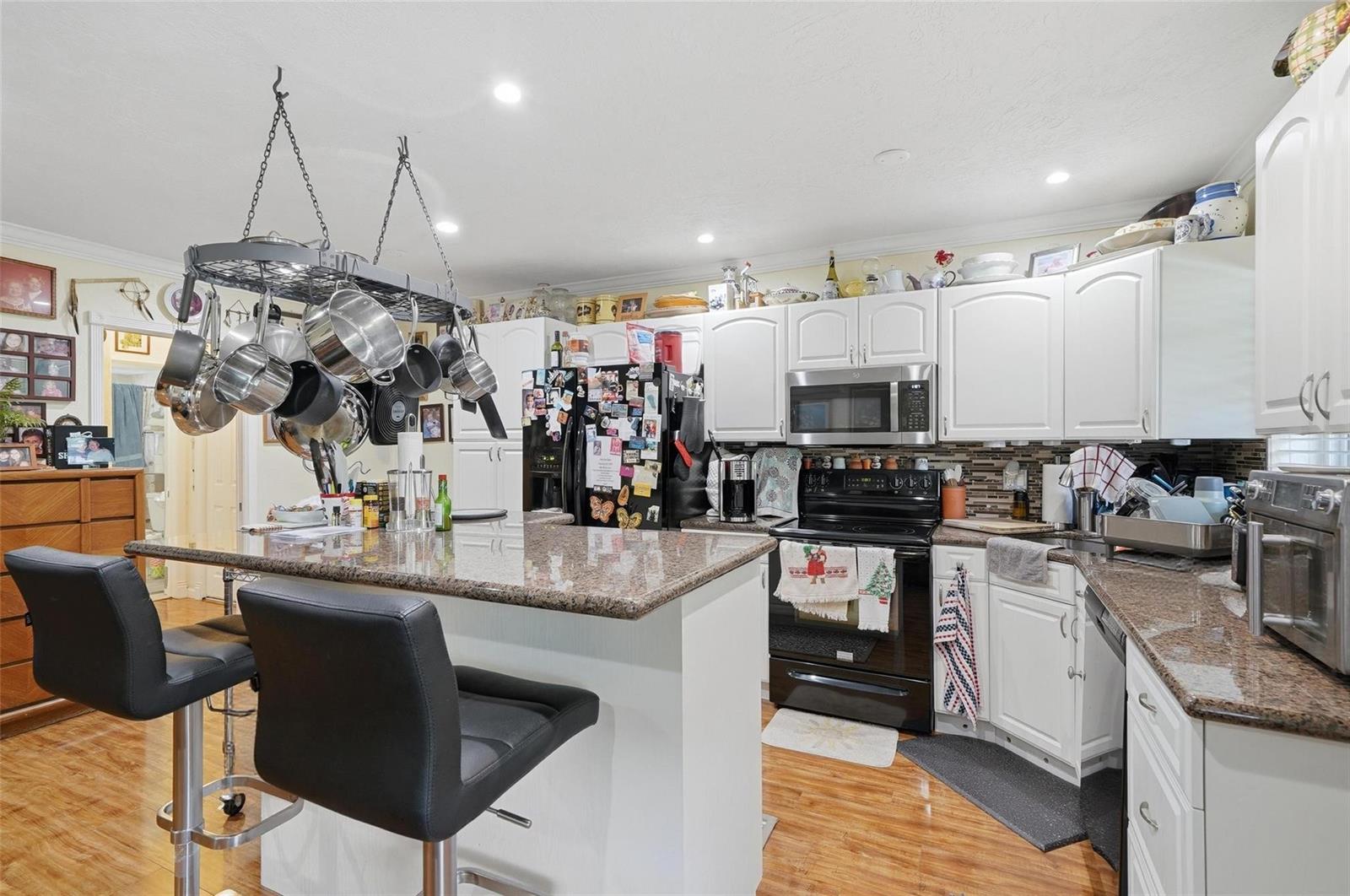 A kitchen features white cabinets, granite countertops, a black stove, and a hanging pot rack — 3510 Harrison Street # 10, Hollywood FL 33021, HOLLYWOOD, FL