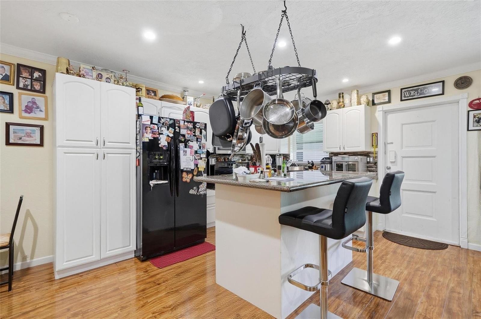 A kitchen features white cabinetry, a black refrigerator, a granite-topped island, and a hanging pot rack — 3510 Harrison Street # 10, Hollywood FL 33021, HOLLYWOOD, FL