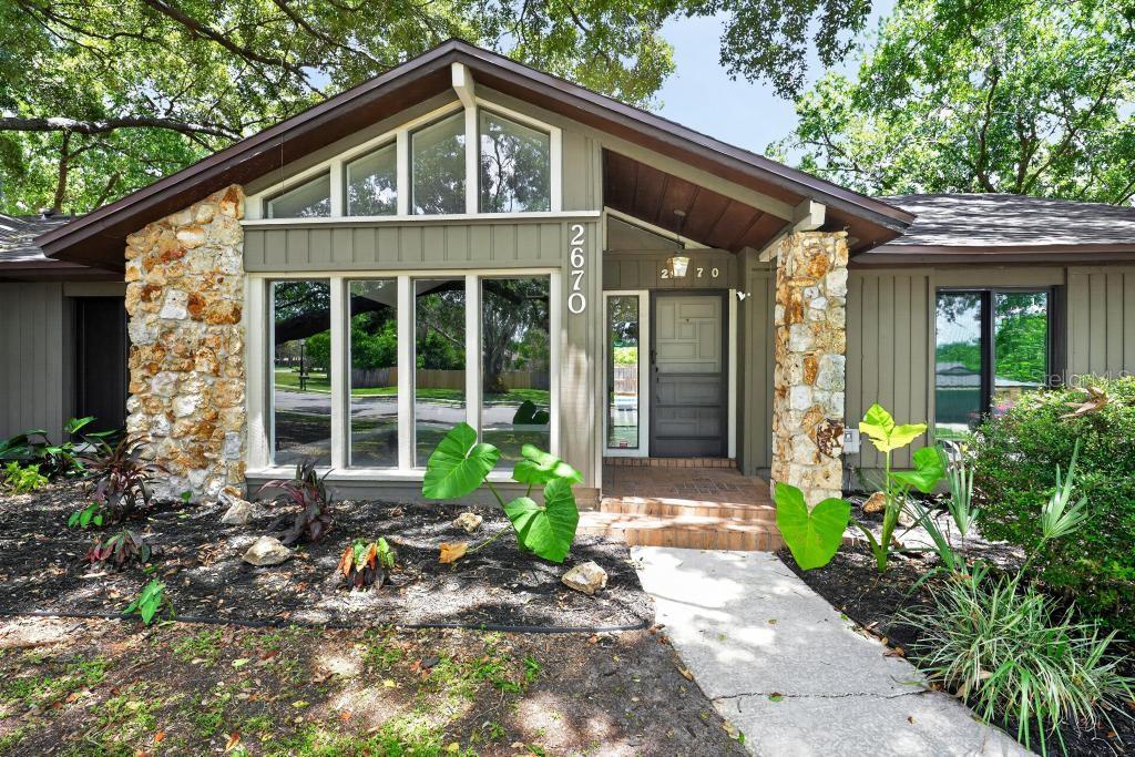 The exterior of a mid-century modern home features stone pillars, vertical siding, and large windows — 2670 JENNIFER HOPE BOULEVARD, LONGWOOD, FL
