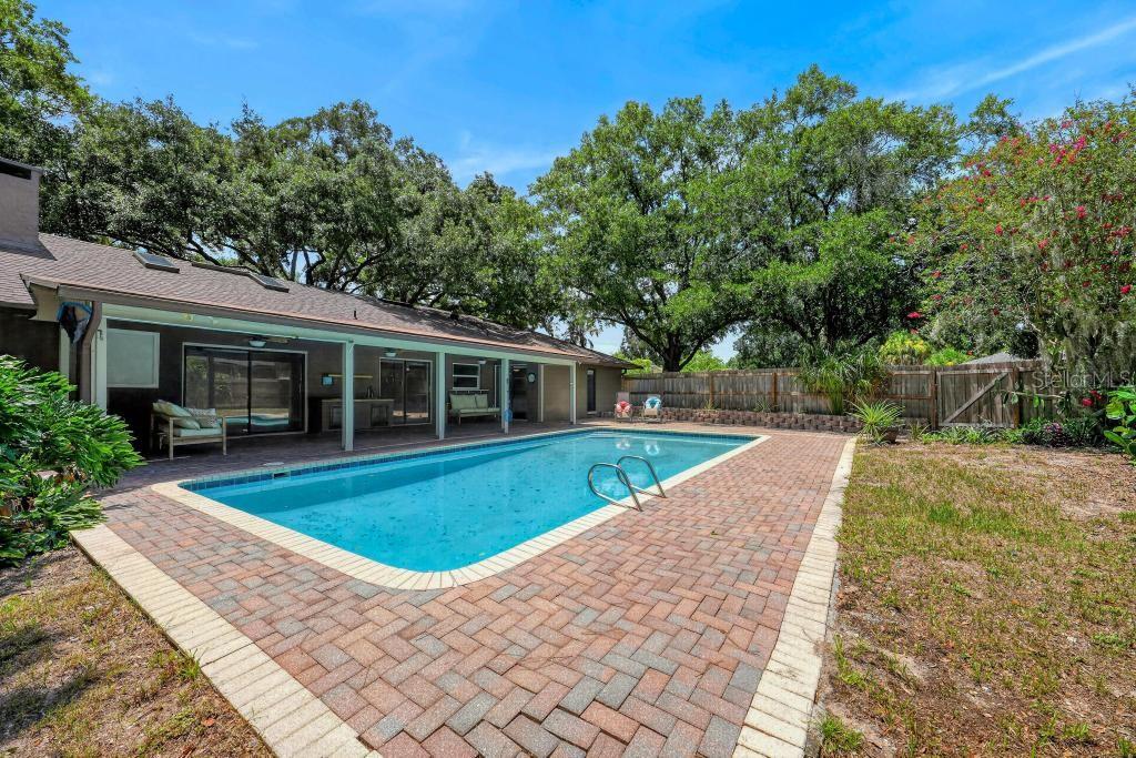 A rectangular swimming pool sits on a brick patio behind a house with a covered porch — 2670 JENNIFER HOPE BOULEVARD, LONGWOOD, FL