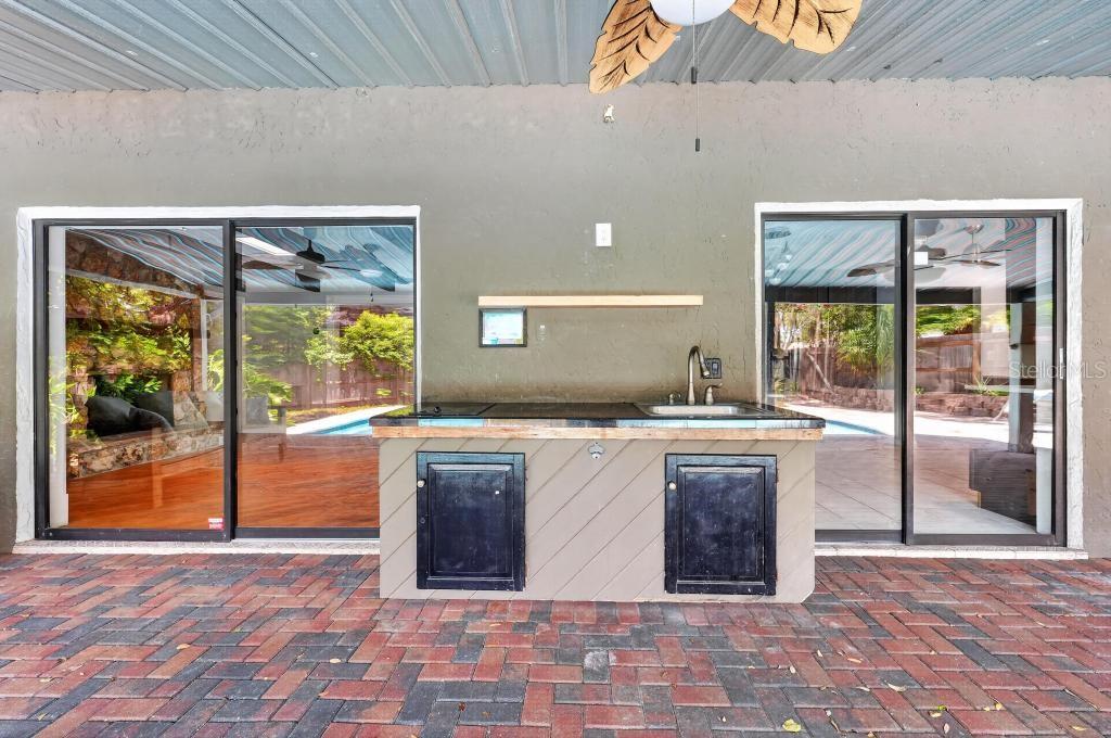 An outdoor kitchen with a sink and black cabinets sits on a brick patio — 2670 JENNIFER HOPE BOULEVARD, LONGWOOD, FL