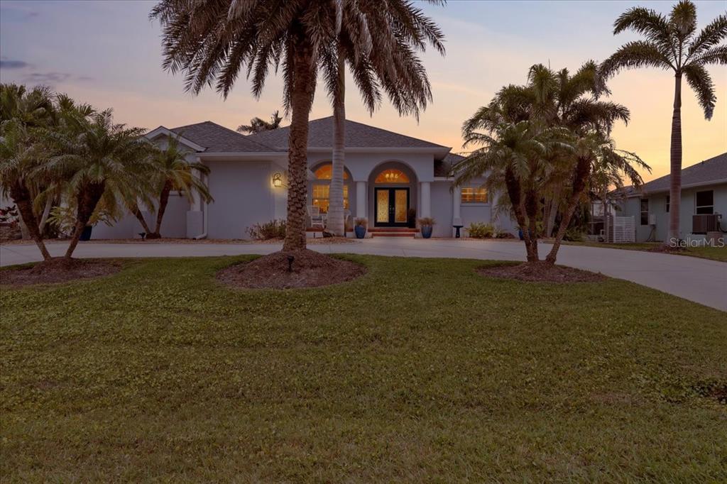 A single-story house with a palm-lined driveway and a central arched entryway at sunset — 1091 ROTONDA CIRCLE, ROTONDA WEST, FL