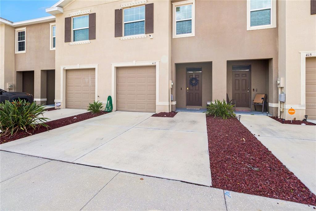 The exterior of a multi-unit townhouse complex features beige stucco walls, brown garage doors, and driveways — 417 NEWMONT CIRCLE, RUSKIN, FL