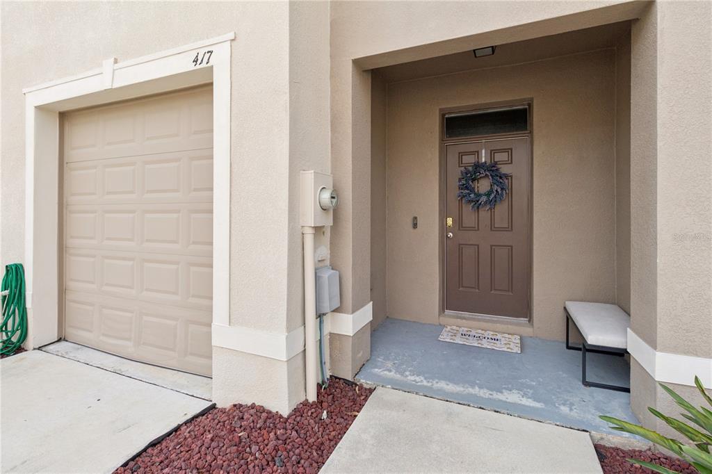 A beige exterior features a single-car garage, a brown front door with a wreath, and a bench — 417 NEWMONT CIRCLE, RUSKIN, FL