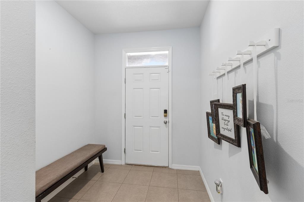 An entryway features a bench, a white door, and framed pictures hanging from a wall rack — 417 NEWMONT CIRCLE, RUSKIN, FL