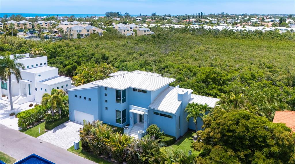 An aerial view shows a light blue two-story house surrounded by lush green trees — 705 JUNGLE QUEEN WAY, LONGBOAT KEY, FL