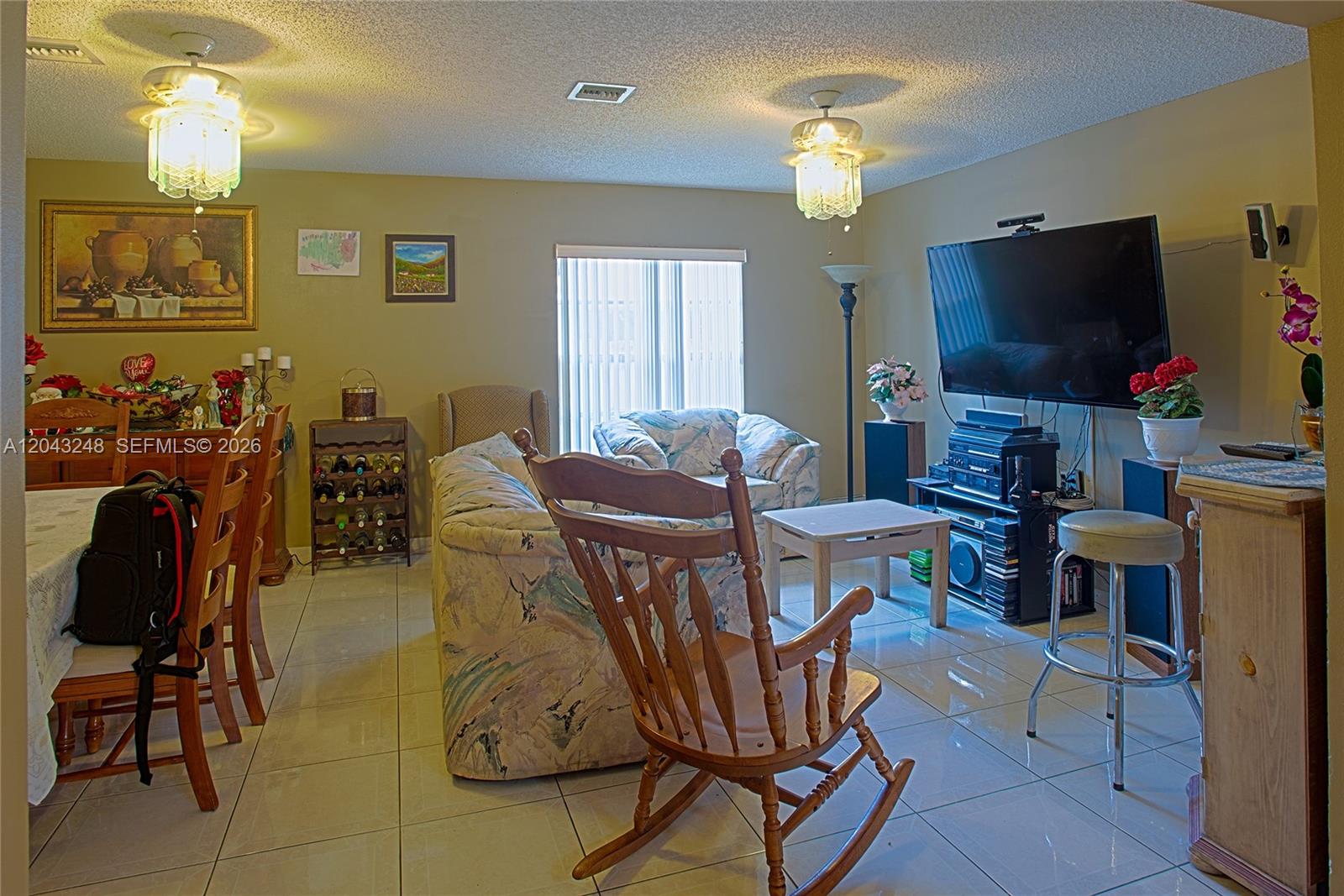 A living and dining area features tile floors, a wooden rocking chair, and two chandeliers — 5889 NW 198th Ter, Hialeah FL 33015, HIALEAH, FL