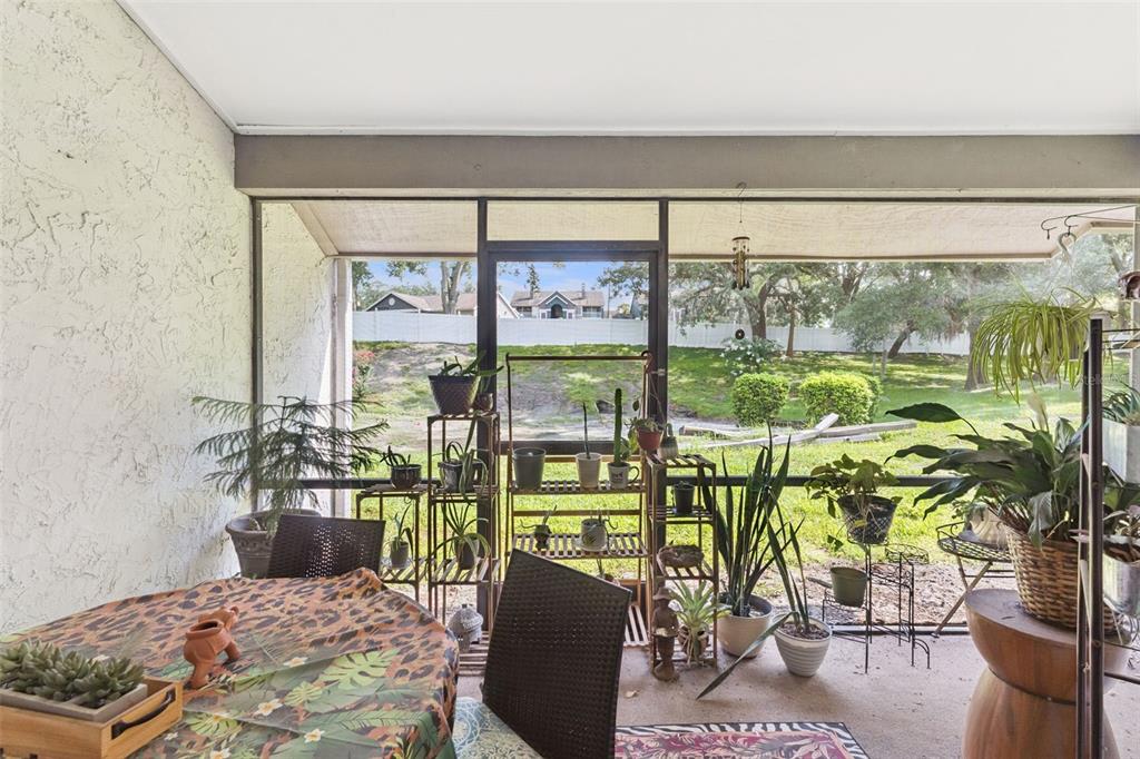 A screened-in patio features a dining table, numerous potted plants, and a view of grass — 145 OLIVE TREE CIRCLE UNIT 145, ALTAMONTE SPRINGS, FL
