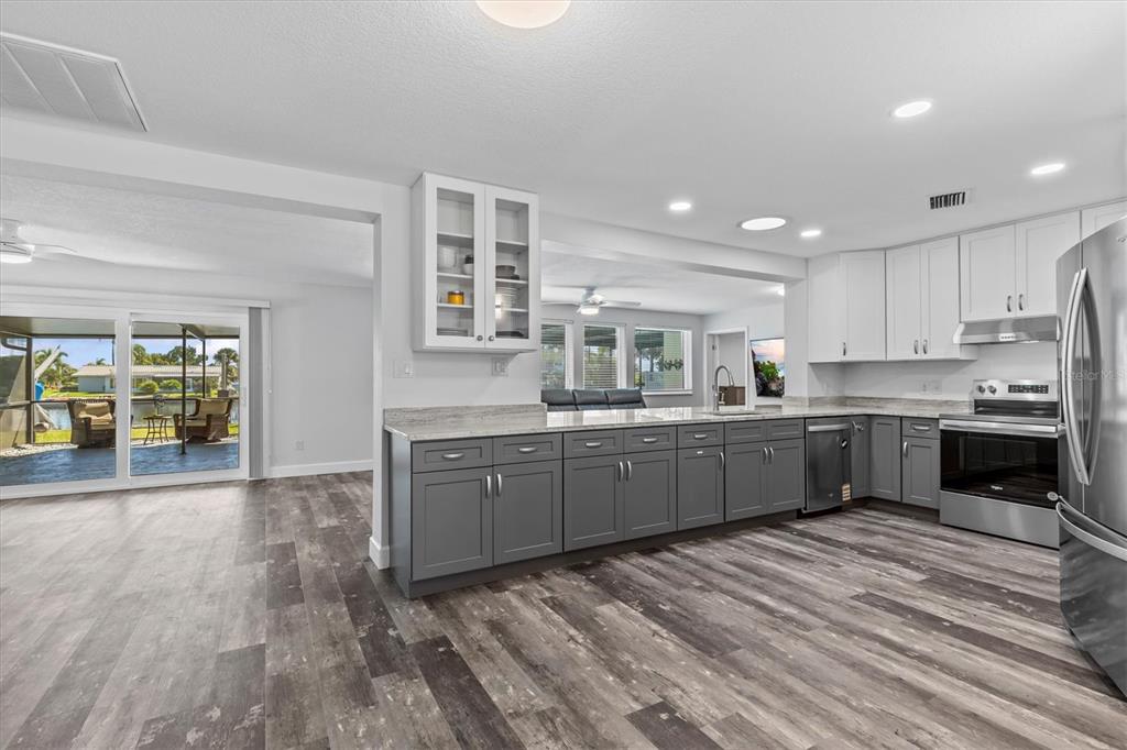 A kitchen with gray lower cabinets, white upper cabinets, and wood-look flooring overlooks a patio — 5524 LEEWARD LANE, NEW PORT RICHEY, FL